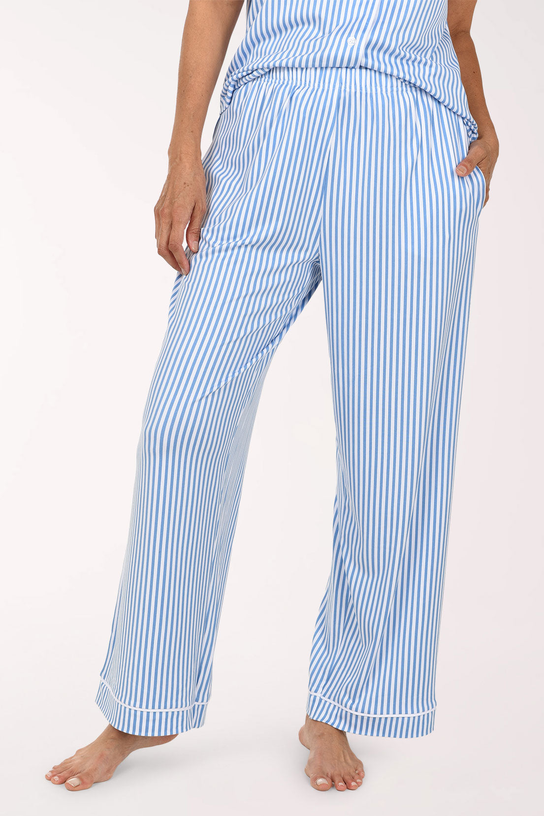 A person wearing light blue and white vertically striped pajama pants with a matching top, shown from the waist down against a plain white studio background.