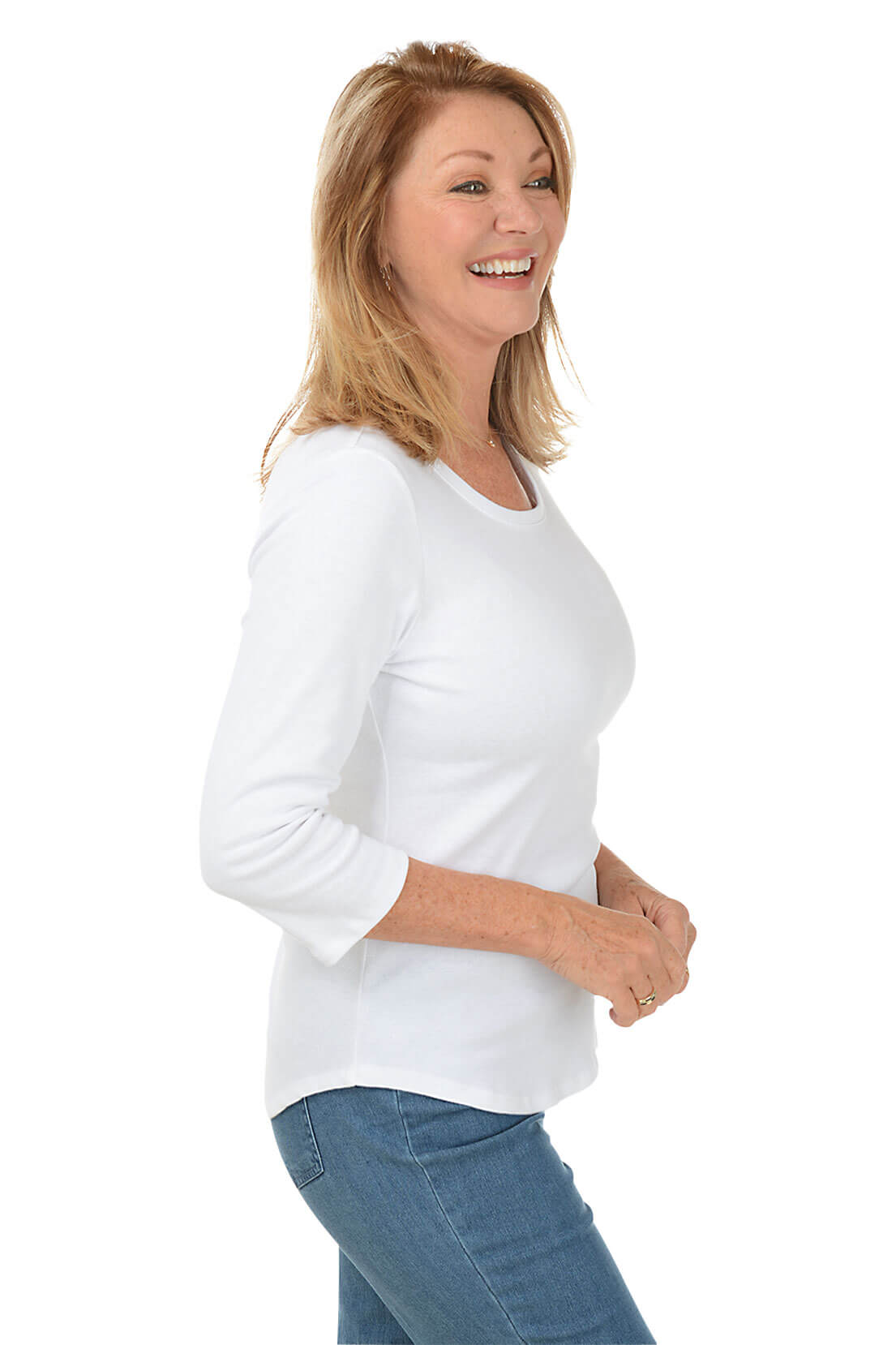 A side shot of a model wearing a white, long-sleeved knit top with a scoop neckline and a curved hemline, paired with blue jeans.