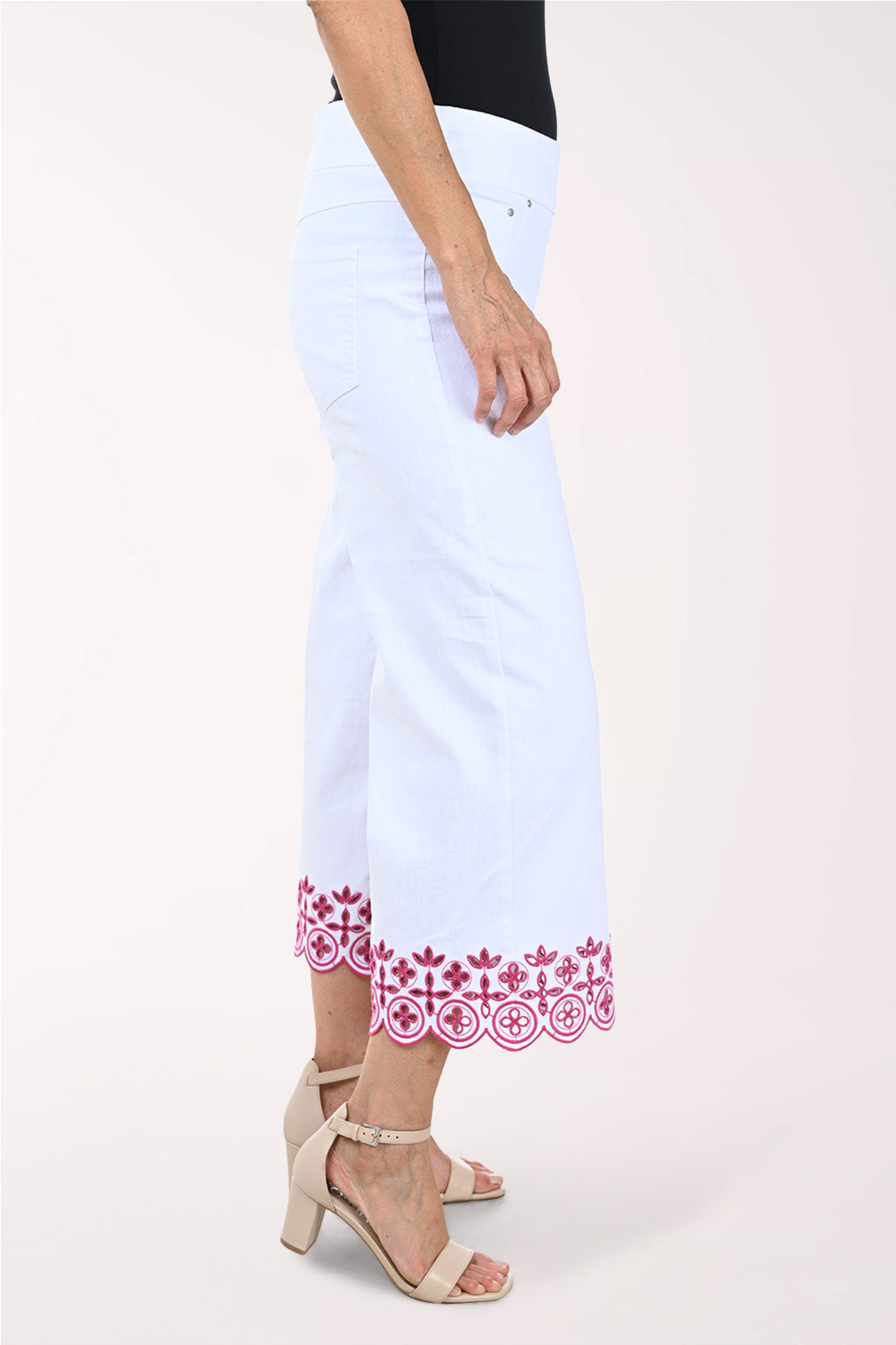 White pants with pink floral embroidery worn by a person on a white background