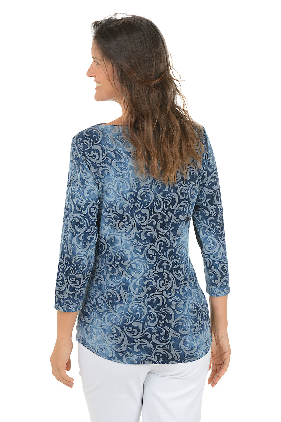 Woman wearing a 3/4 sleeve blue tie-dye indigo scroll patterned top and white pants on a white background. Back shot.
