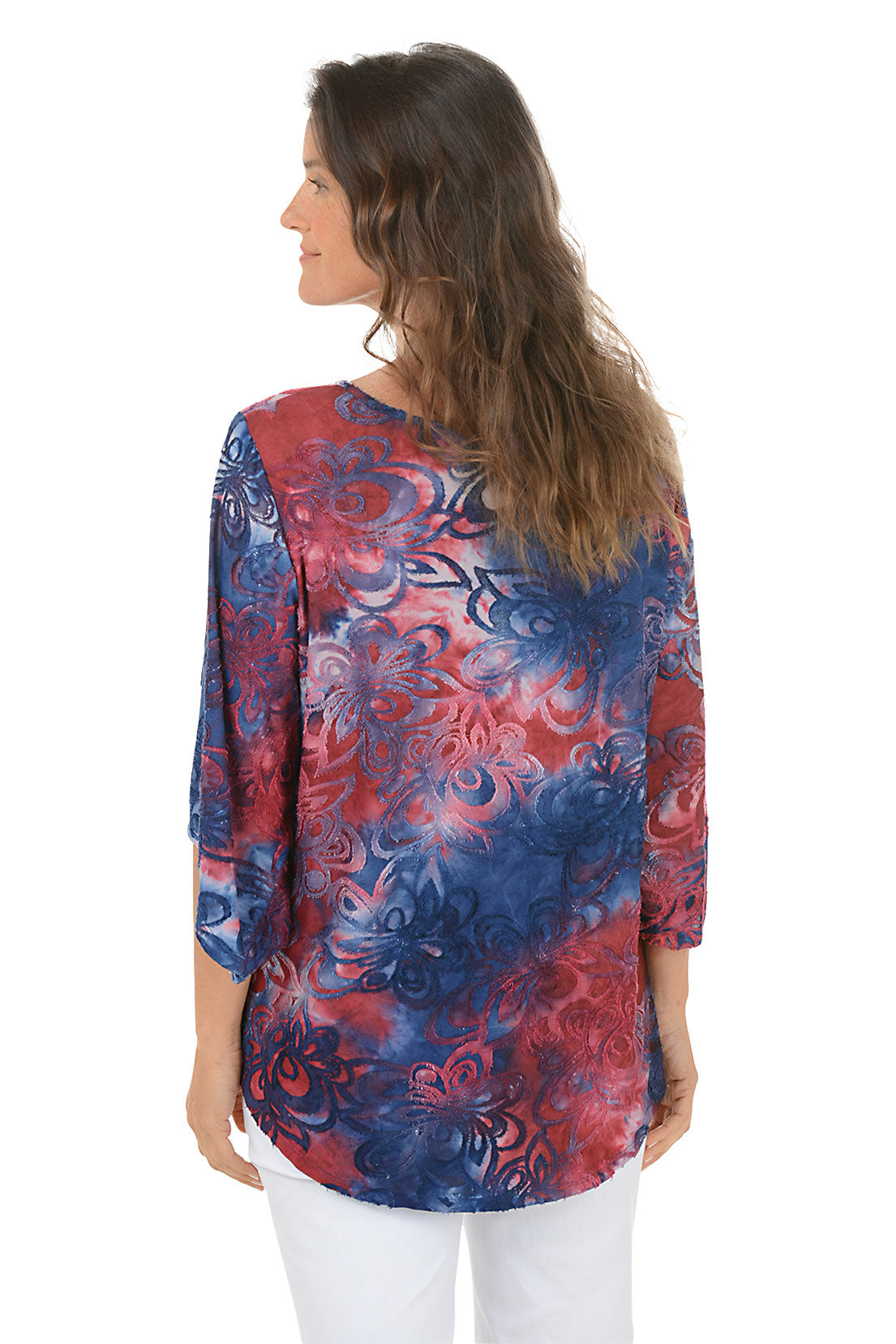 Woman wearing a colorful red and blue floral blouse with white pants on a white background. Back shot.