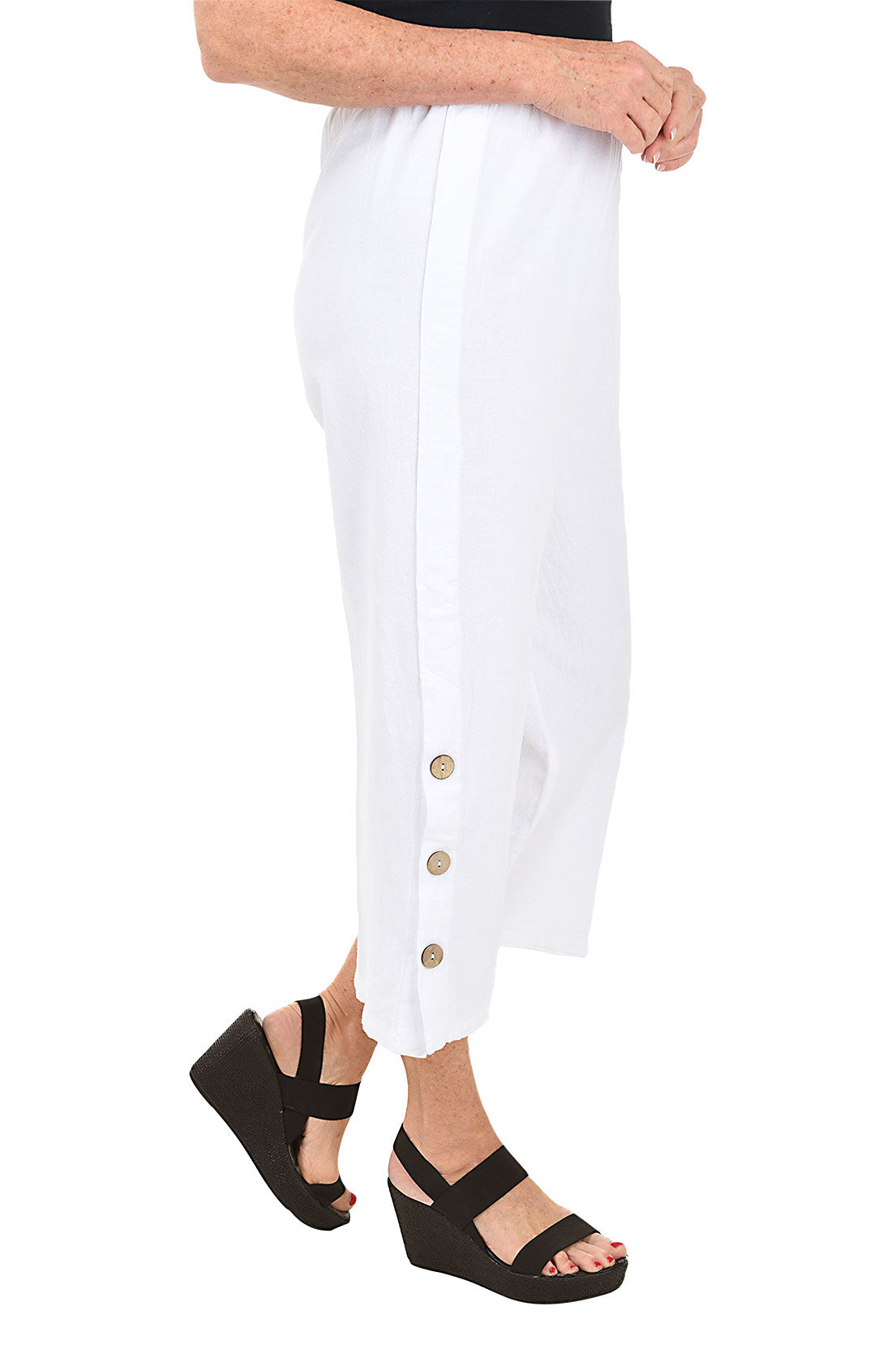 A side shot of a model wearing a pair of white capri pants with side button detail on the hemline, made of crinkle cotton fabric.