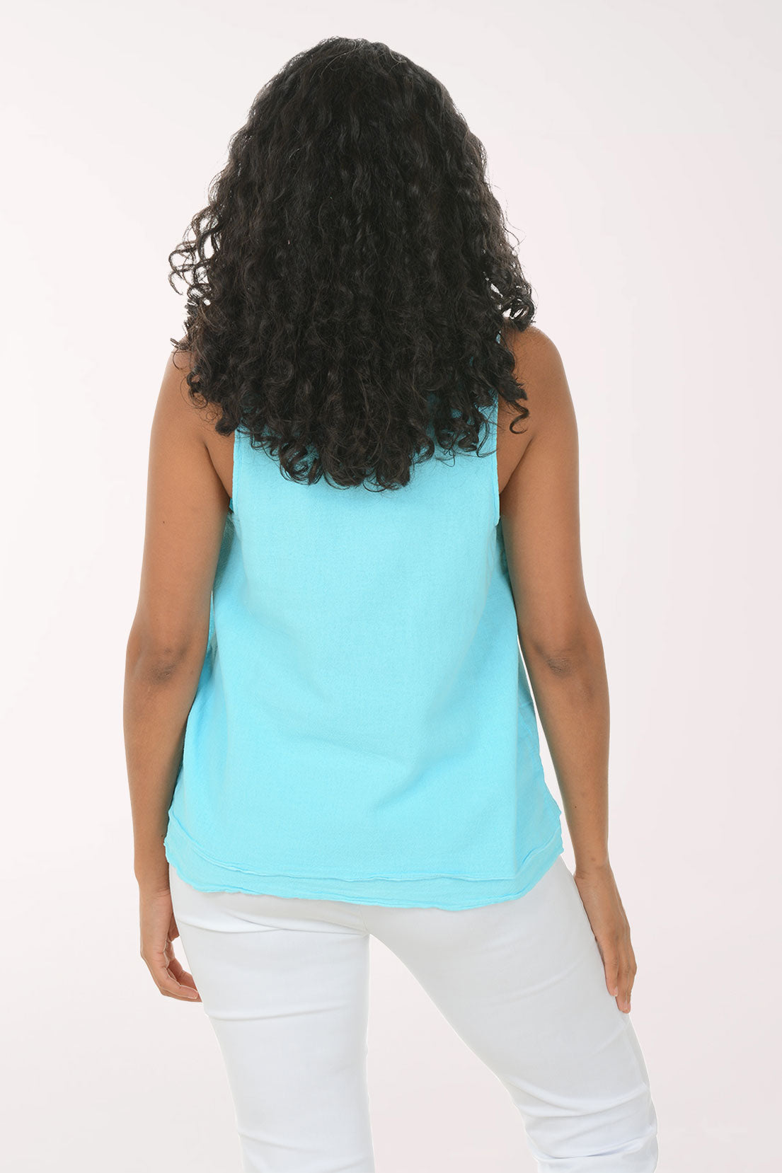 Woman wearing a light blue sleeveless top and white pants on a white background