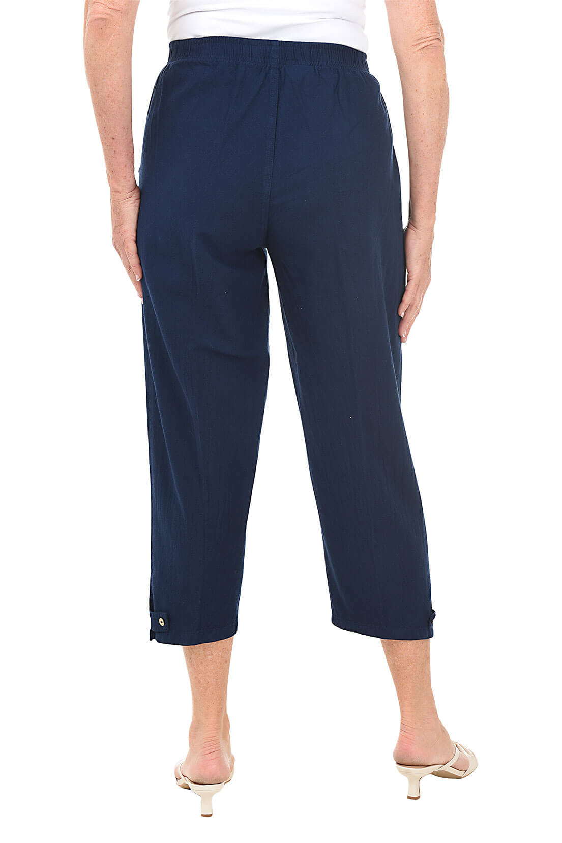 A back shot of a model wearing a pair of navy blue capri pants with button-tab detail on the hemline, made of crinkle cotton fabric, with an elastic waistband and side pockets.