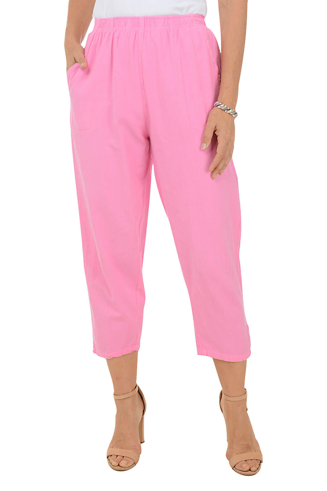A front shot of a model wearing a pair of pink capri pants with button-tab detail on the hemline, made of crinkle cotton fabric, with an elastic waistband and side pockets.