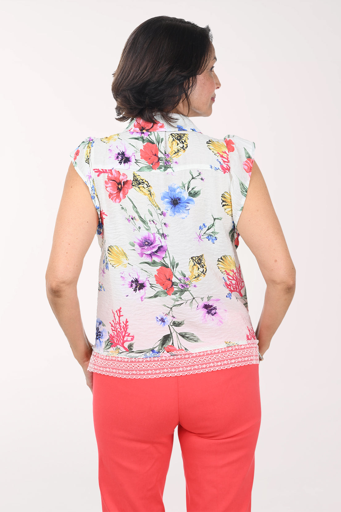 Woman wearing a sleeveless floral blouse with red pants on a white background
