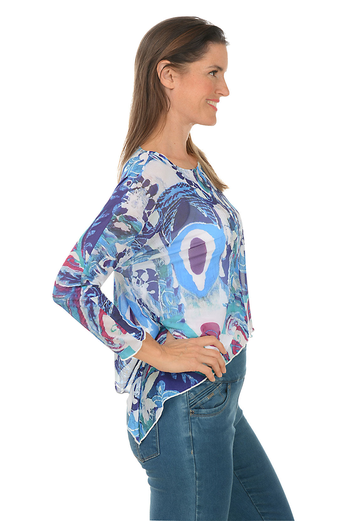 A side shot of a model wearing a multicolored floral asymmetrical top with long sleeves and a scoop neckline, paired with blue jeans.