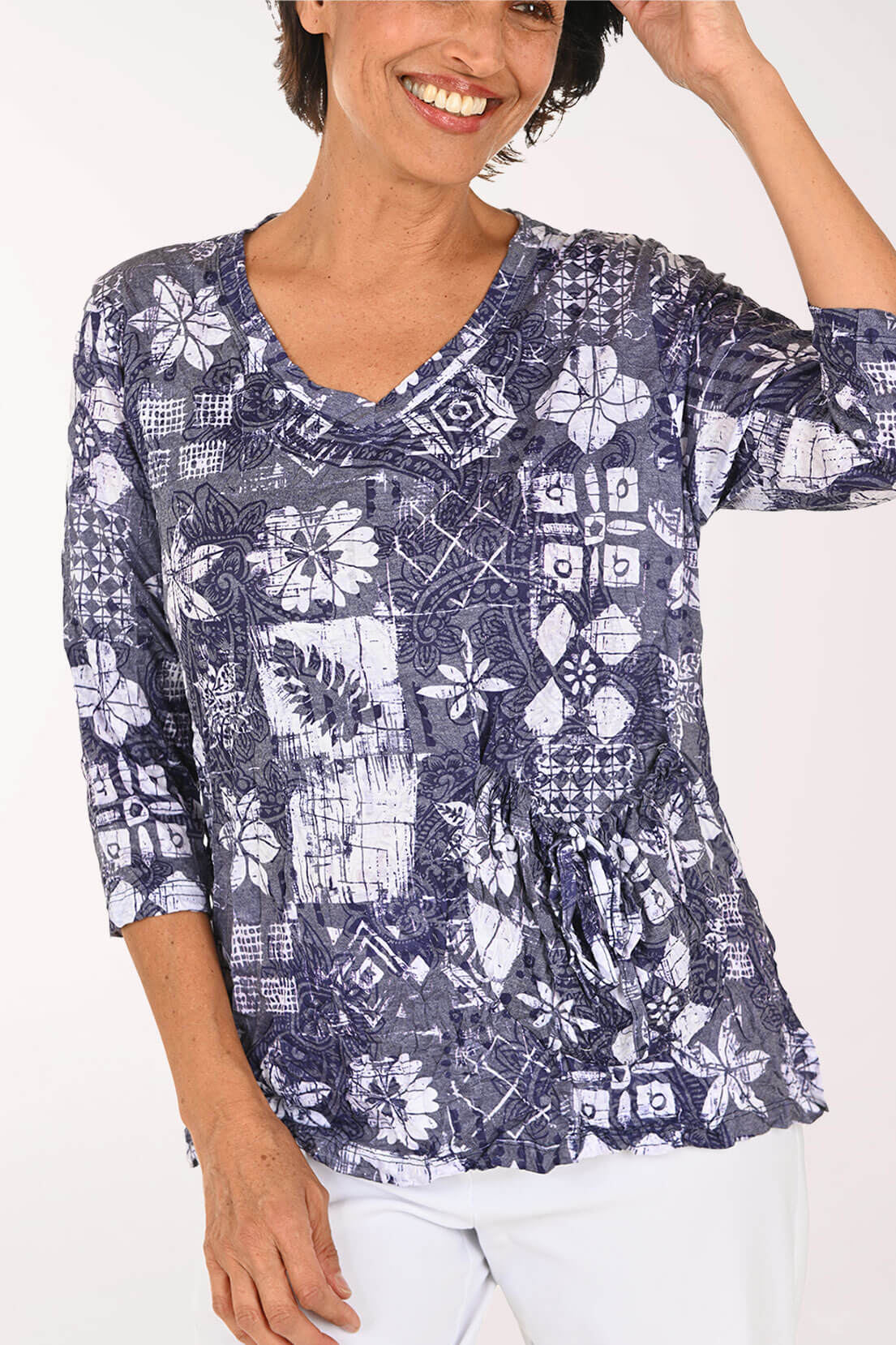 A woman wearing a navy blue and white patterned three-quarter sleeve top with a V-neck and gathered waist, paired with white pants, against a plain white background.