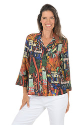 Woman wearing a colorful patterned blouse with white pants on a white background.