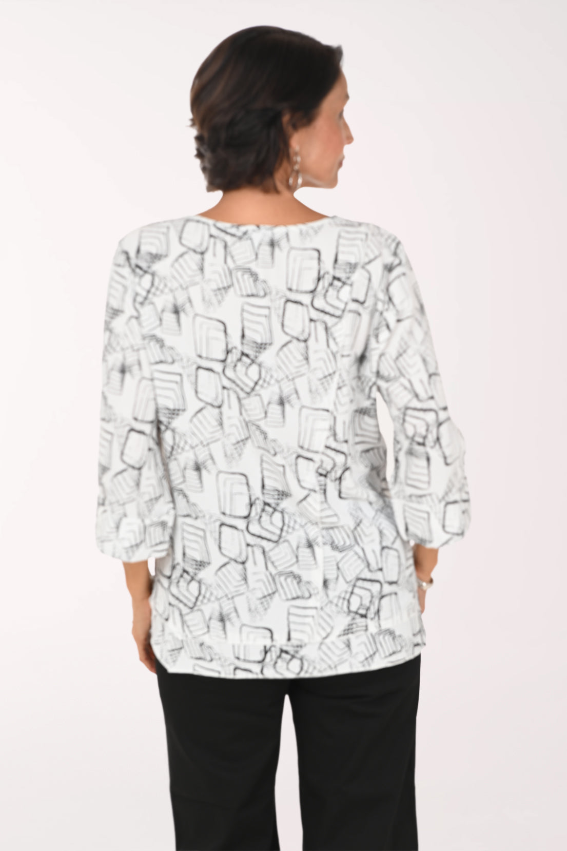 A woman modeling a white three-quarter sleeve top with a black abstract line print, paired with black pants, against a plain white background.