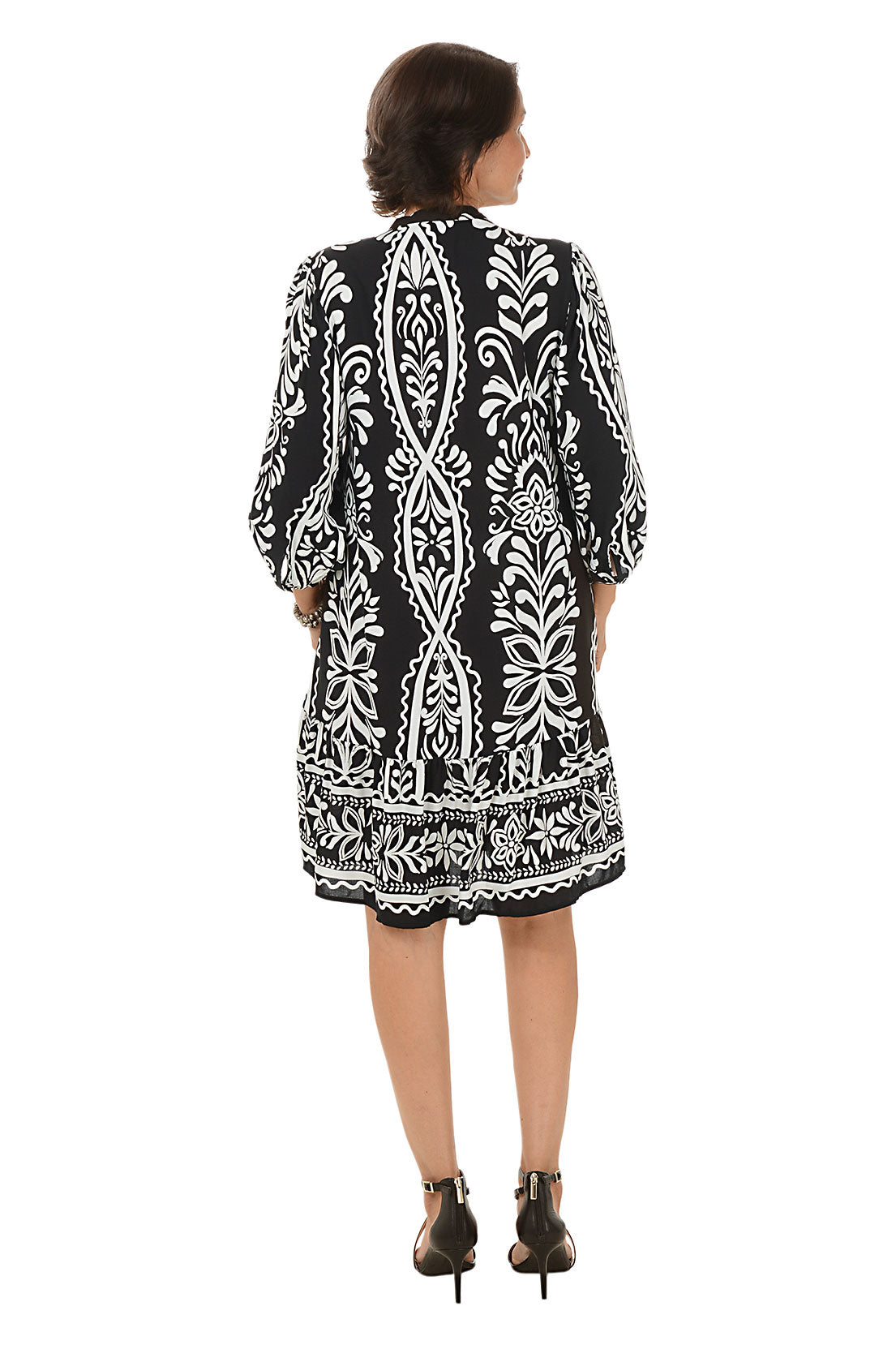 Woman wearing a black and white patterned dress on a white background. Back shot.