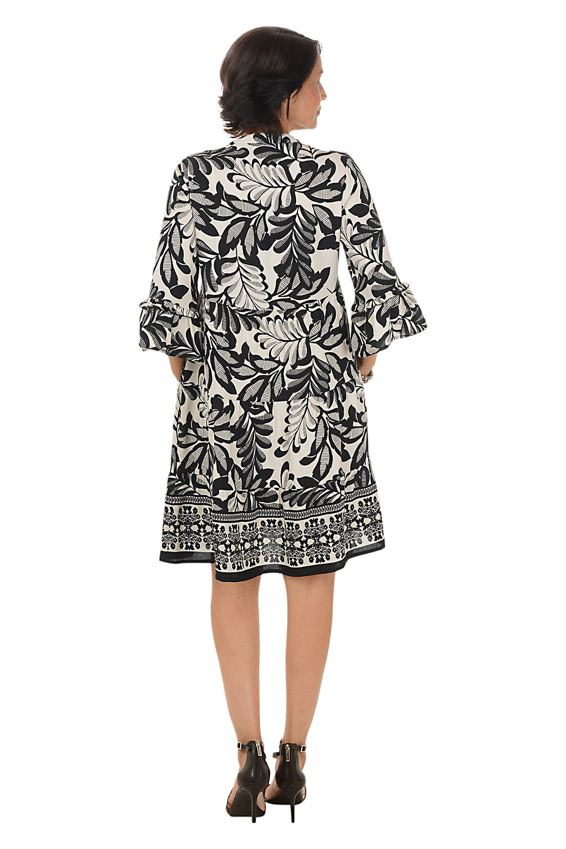 Woman wearing a black and white patterned dress on a white background. Back shot.