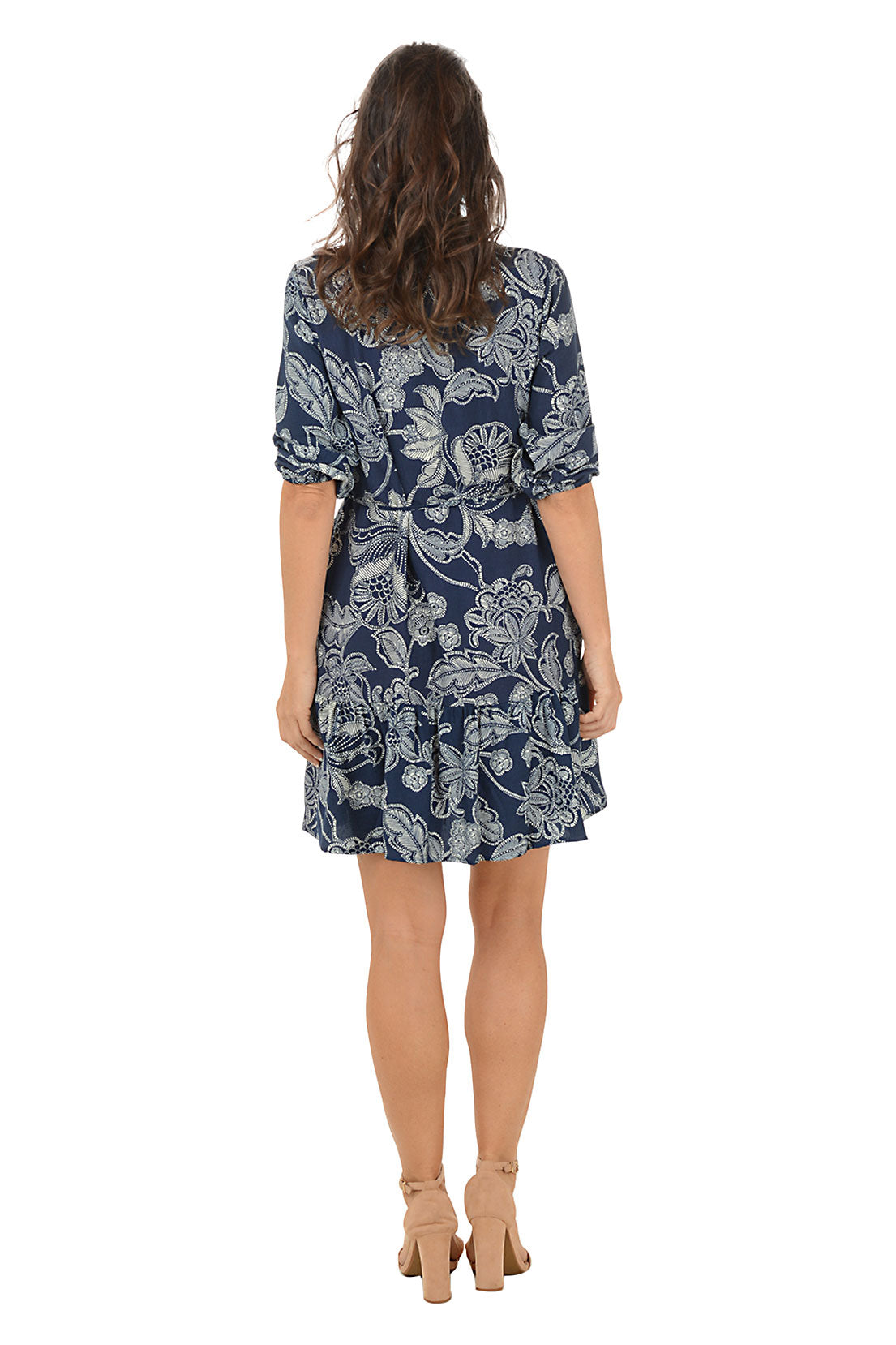 Woman wearing a 3/4 sleeve navy floral patterned dress with roll-up sleeves and a collar. Back shot.