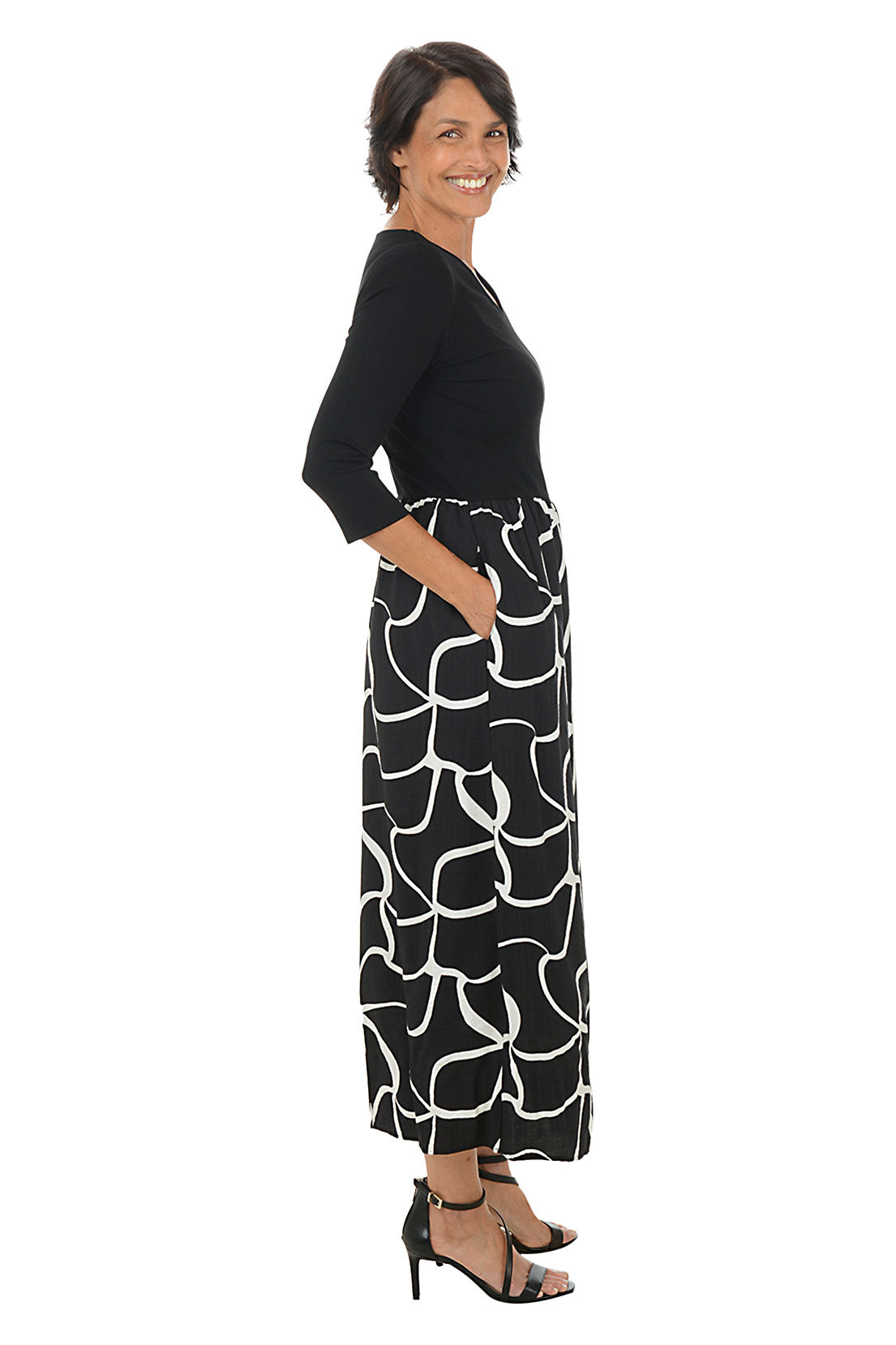Woman wearing a 3/4 sleeve black and white patterned maxi dress on a white background. Back shot.