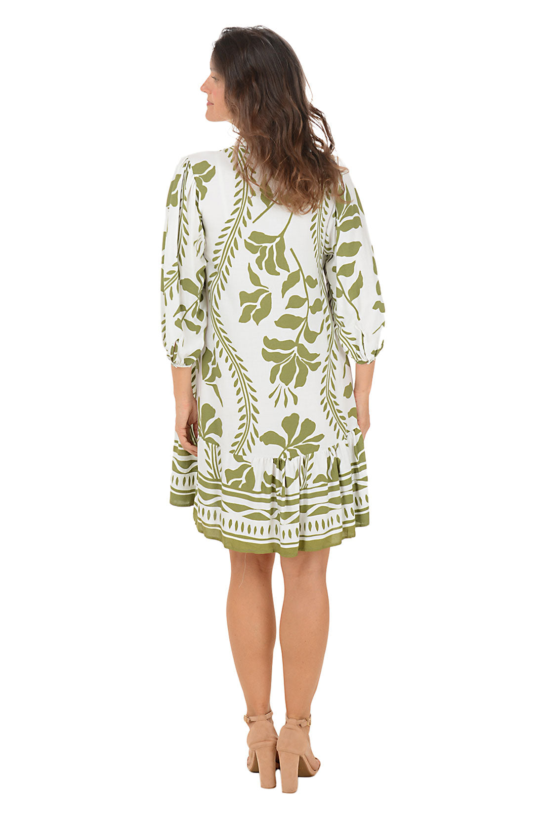 Woman wearing a 3/4 sleeved green and white floral vine patterned dress on a white background. Back shot.