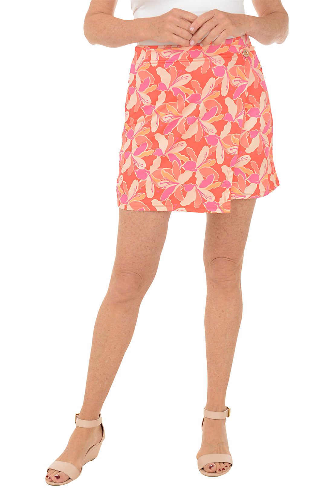 A front shot of a model wearing a pink and orange geometric patterned Stella Parker wrap skort with a gold button detail, side zipper pockets, and an asymmetrical hemline.