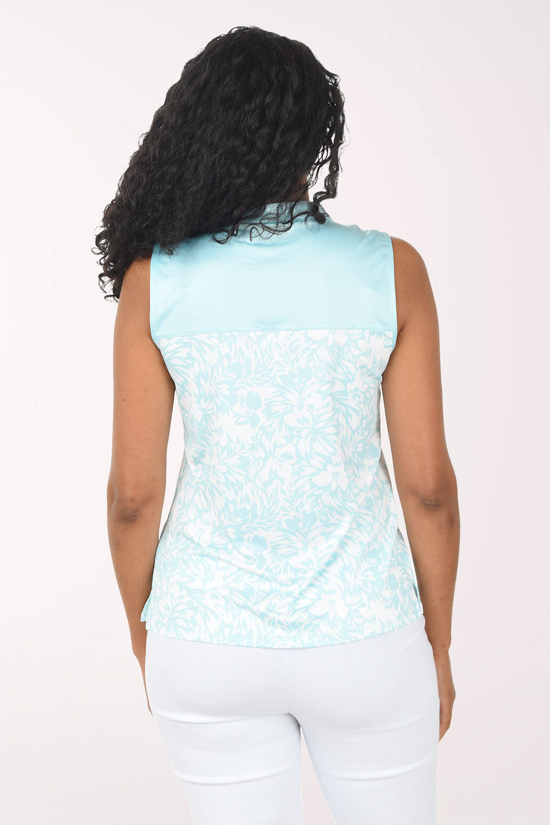 Woman wearing a light blue sleeveless patterned top and white pants on a white background