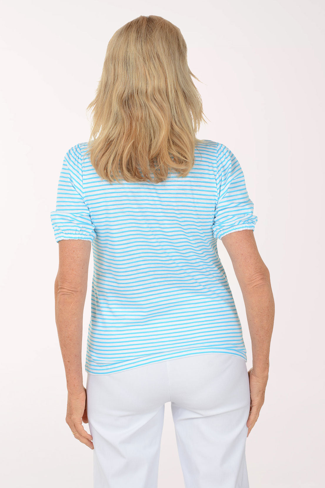 Woman wearing a light blue striped shirt and white pants on a white background