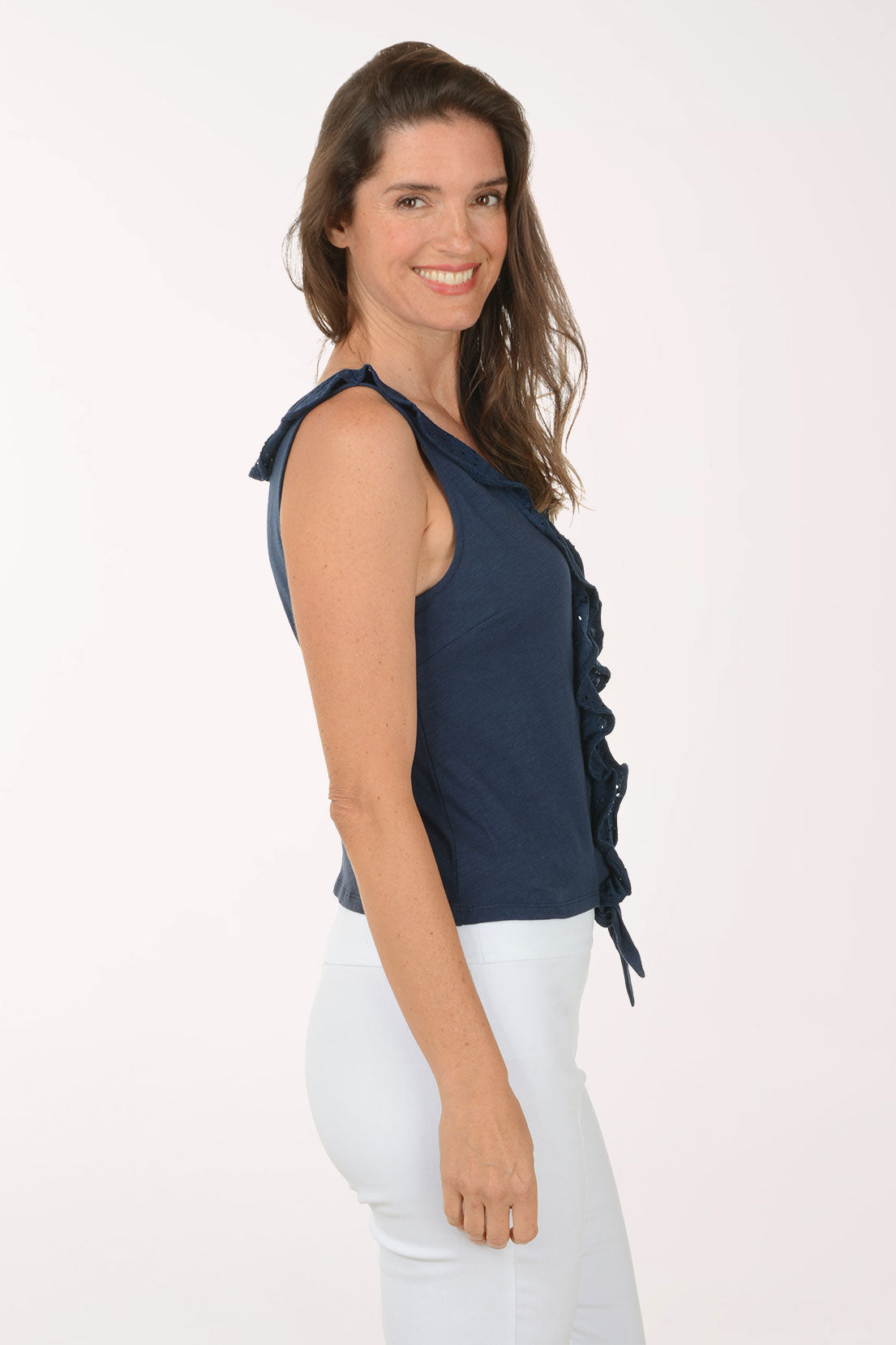 Woman wearing a navy blue sleeveless top with a tie detail and white pants on a light pink background