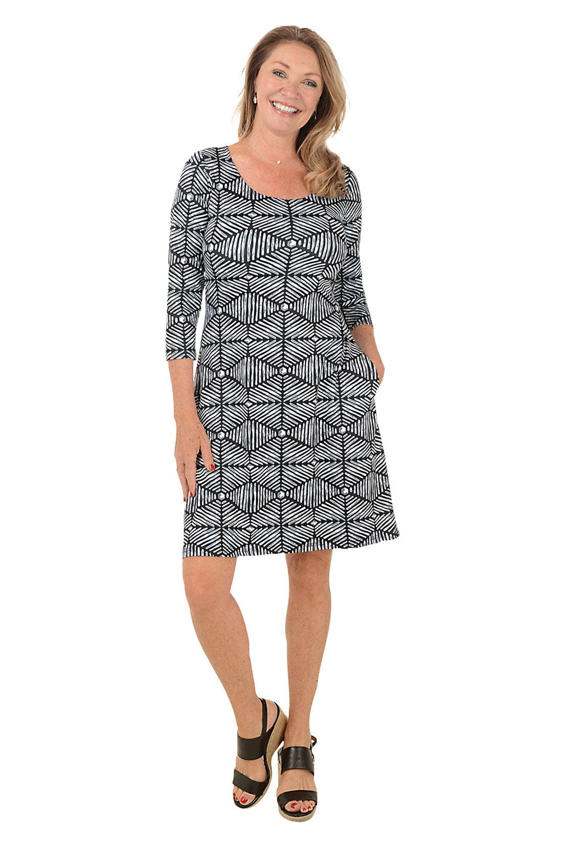 A front shot of a model wearing a knee-length, 3/4 sleeve black and white geometric pattern dress with a scoop neckline and dual side pockets.