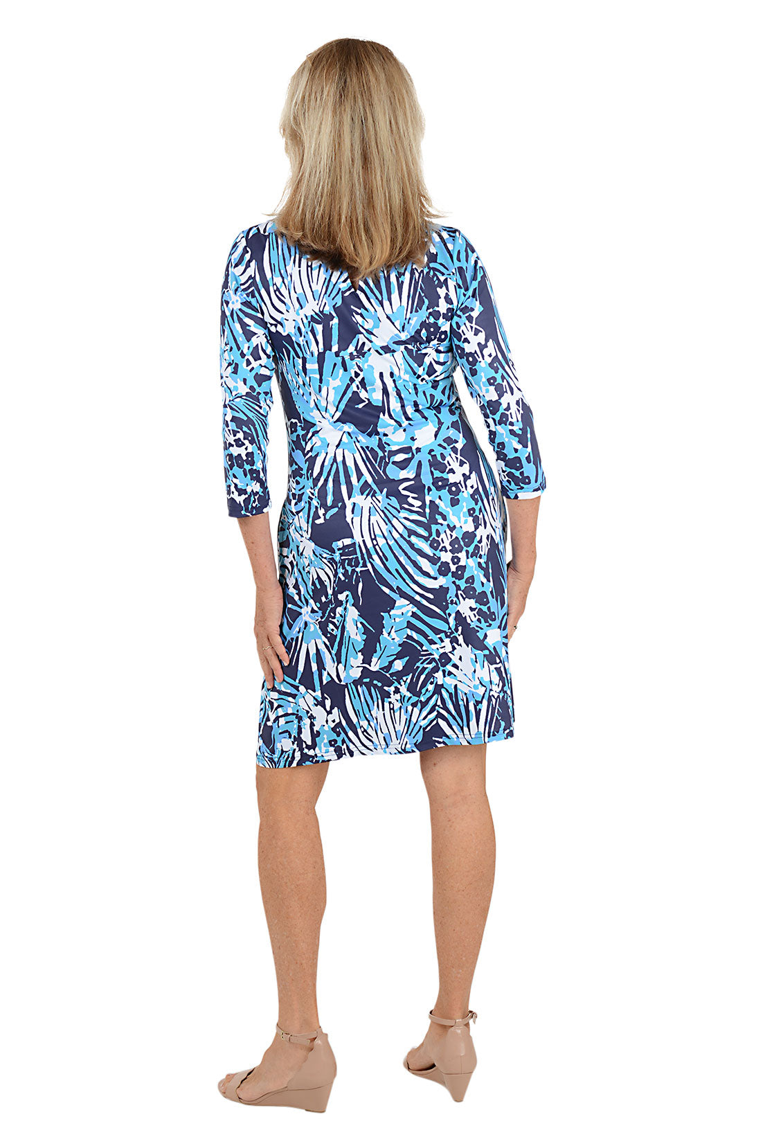 Woman wearing a blue and white abstract leaf patterned dress on a white background. Back shot.