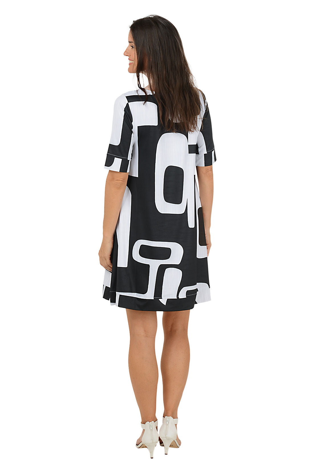 Woman wearing a 3/4 sleeve black and white abstract patterned swing dress on a white background. Back shot.