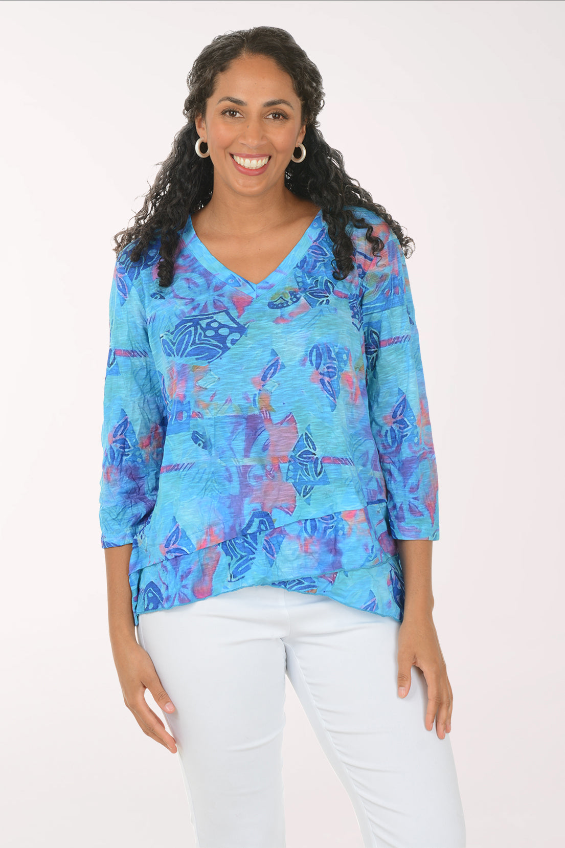 Woman wearing a blue patterned blouse with white pants on a white background
