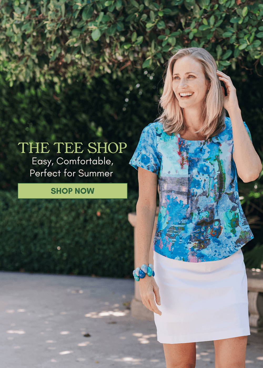Model posing in a multi tee in front in a garden.