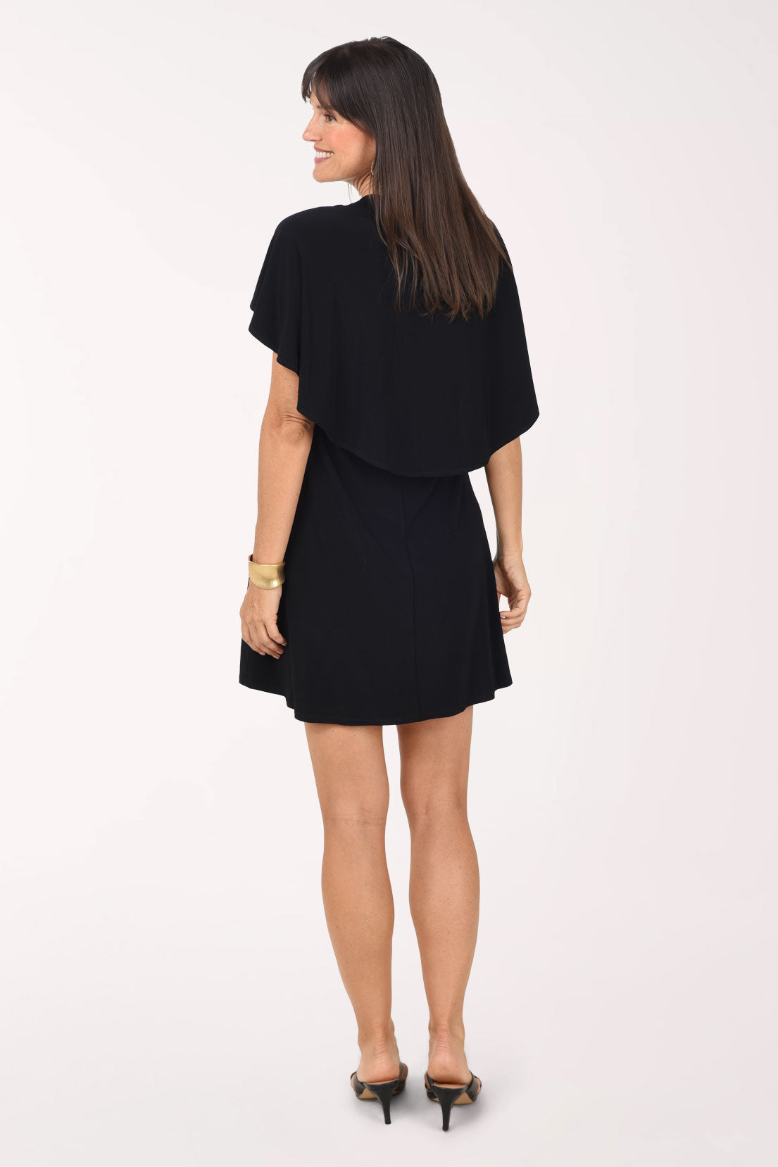 Back view of the black Cold Shoulder Cape Dress showing the cape layer draping across the shoulders and upper back over the fitted dress, worn with black heeled sandals