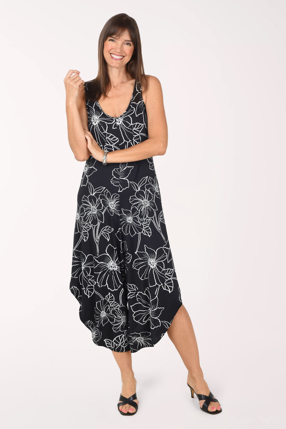 Front view of the Black Floral jumpsuit with legs together, showing how the wide legs and curved hems fall like a midi skirt, worn with black heeled sandals