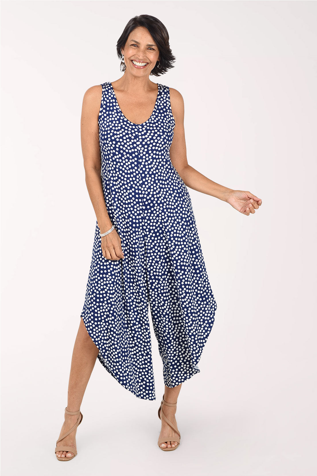 Front view of the navy polka dot jumpsuit in motion, showing the two wide legs separating with pointed, angled hems