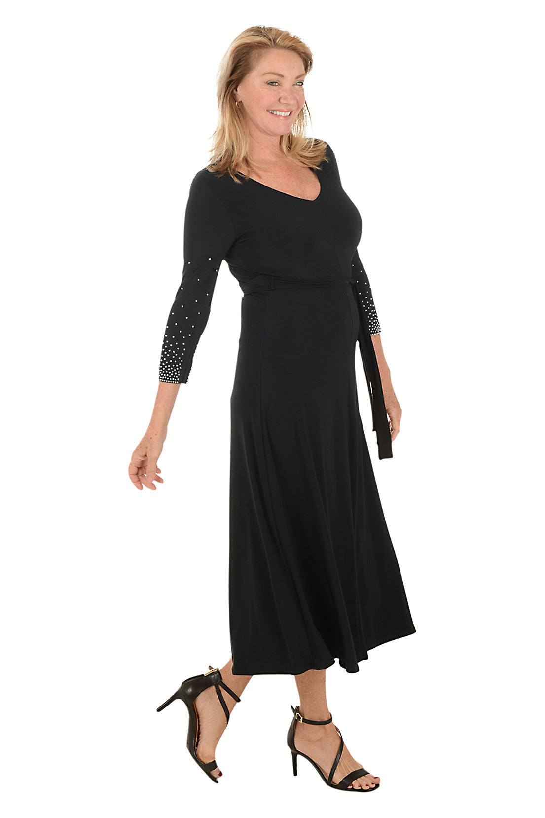 Woman wearing a black dress with embellished sleeves on a white background. Side shot.