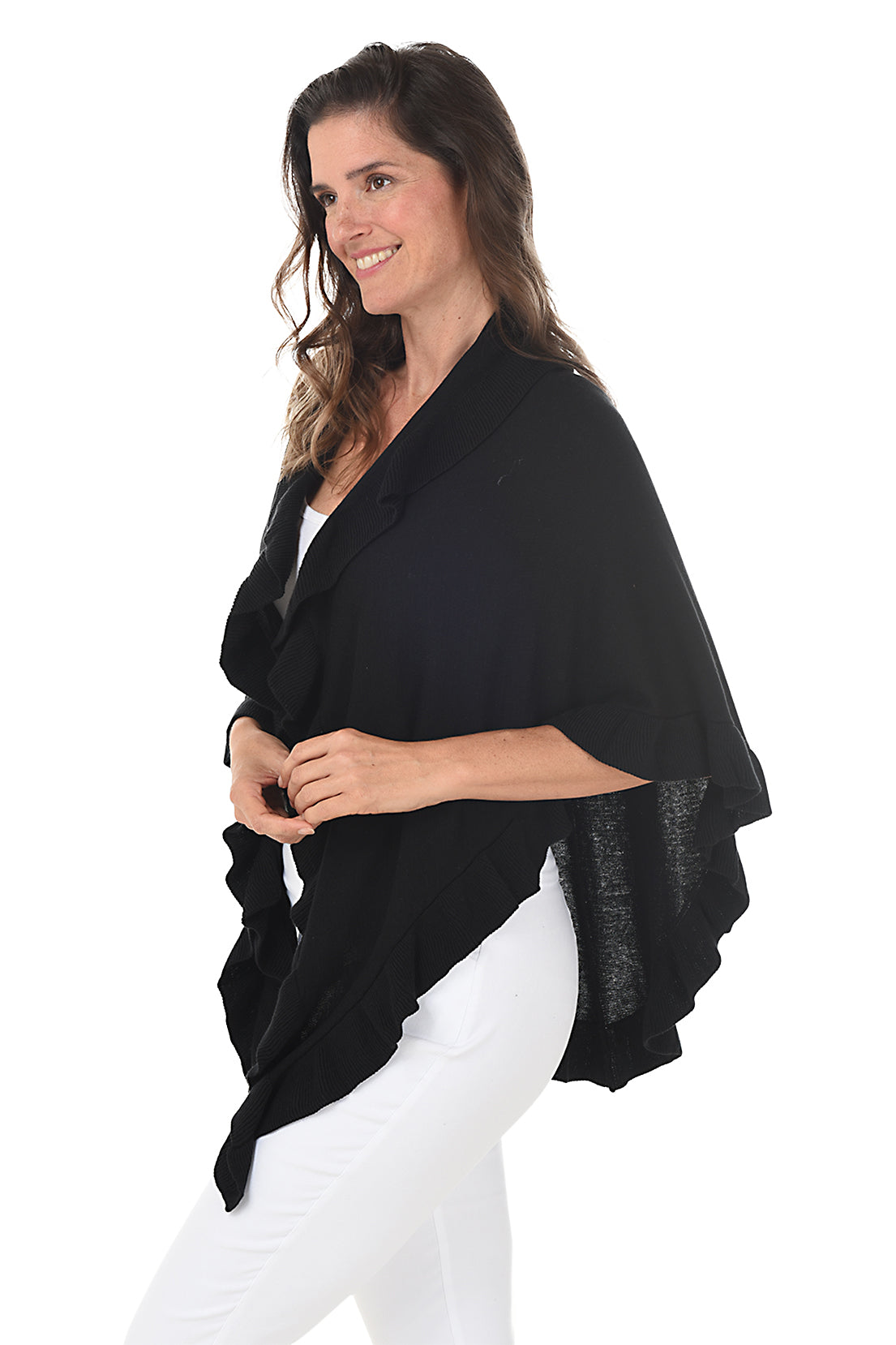 A woman wearing a black open front wrap sweater with ruffled rib-knit trim over a white top and white pants. Side shot.