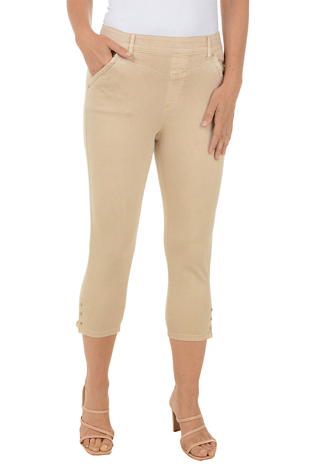A front shot of a model wearing a pair of beige denim capri pants with a stretch waistband, belt loops, dual front pockets, and triple studded detail on the hemline.