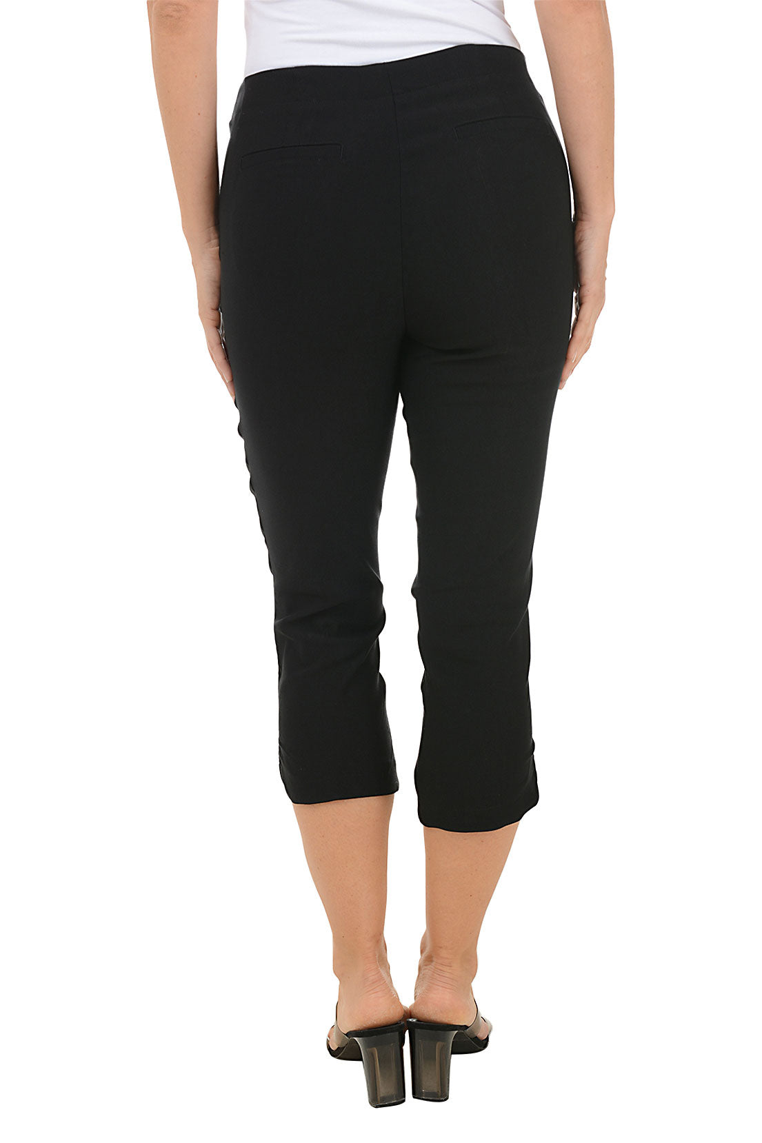 A back shot of a model wearing a pair of black capri pants with a stretch waistband and tummy control lining, featuring dual front pockets and a tulip hemline.