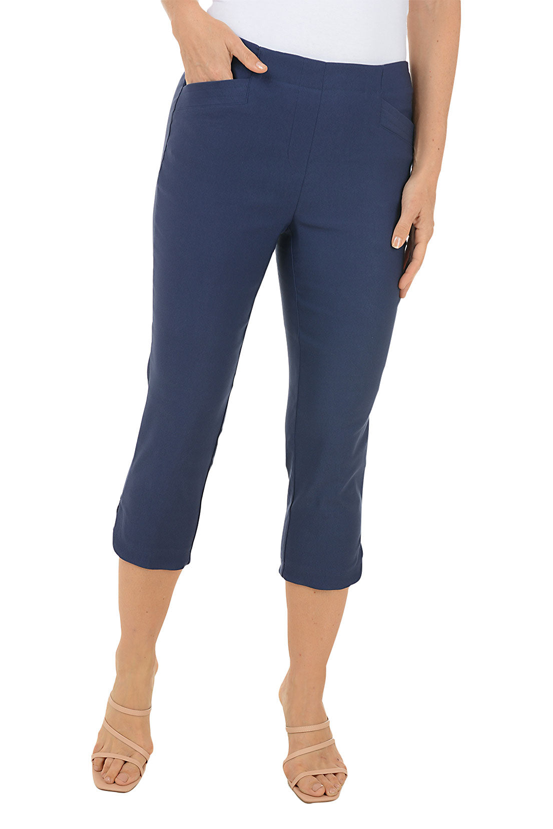 A front shot of a model wearing a pair of navy capri pants with a stretch waistband and tummy control lining, featuring dual front pockets and a tulip hemline.