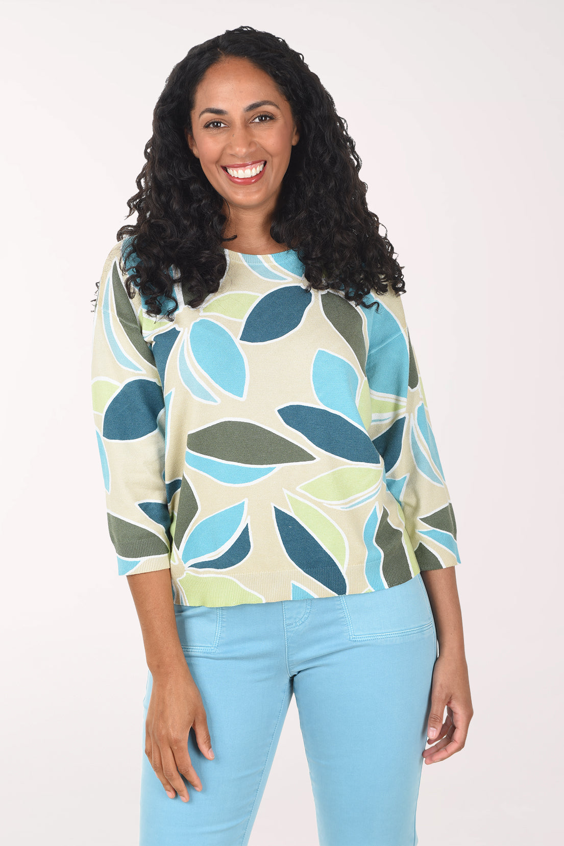 Woman wearing a patterned sweater and light blue jeans on a white background