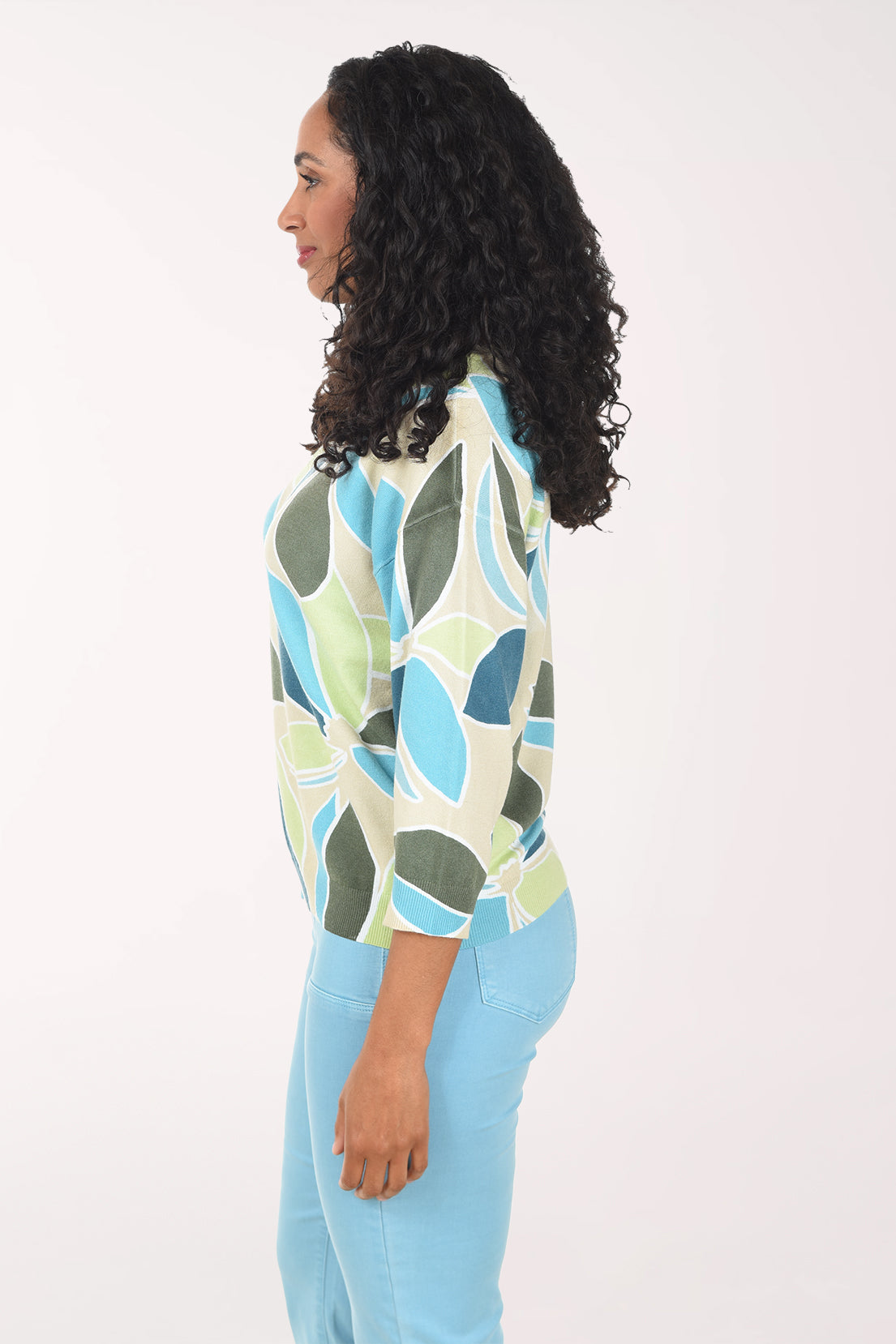 Woman wearing a patterned sweater and light blue jeans on a white background