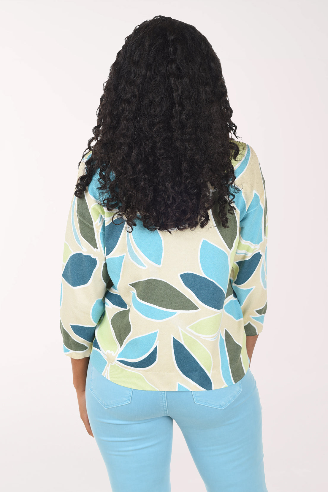 Woman wearing a patterned sweater and light blue jeans on a white background