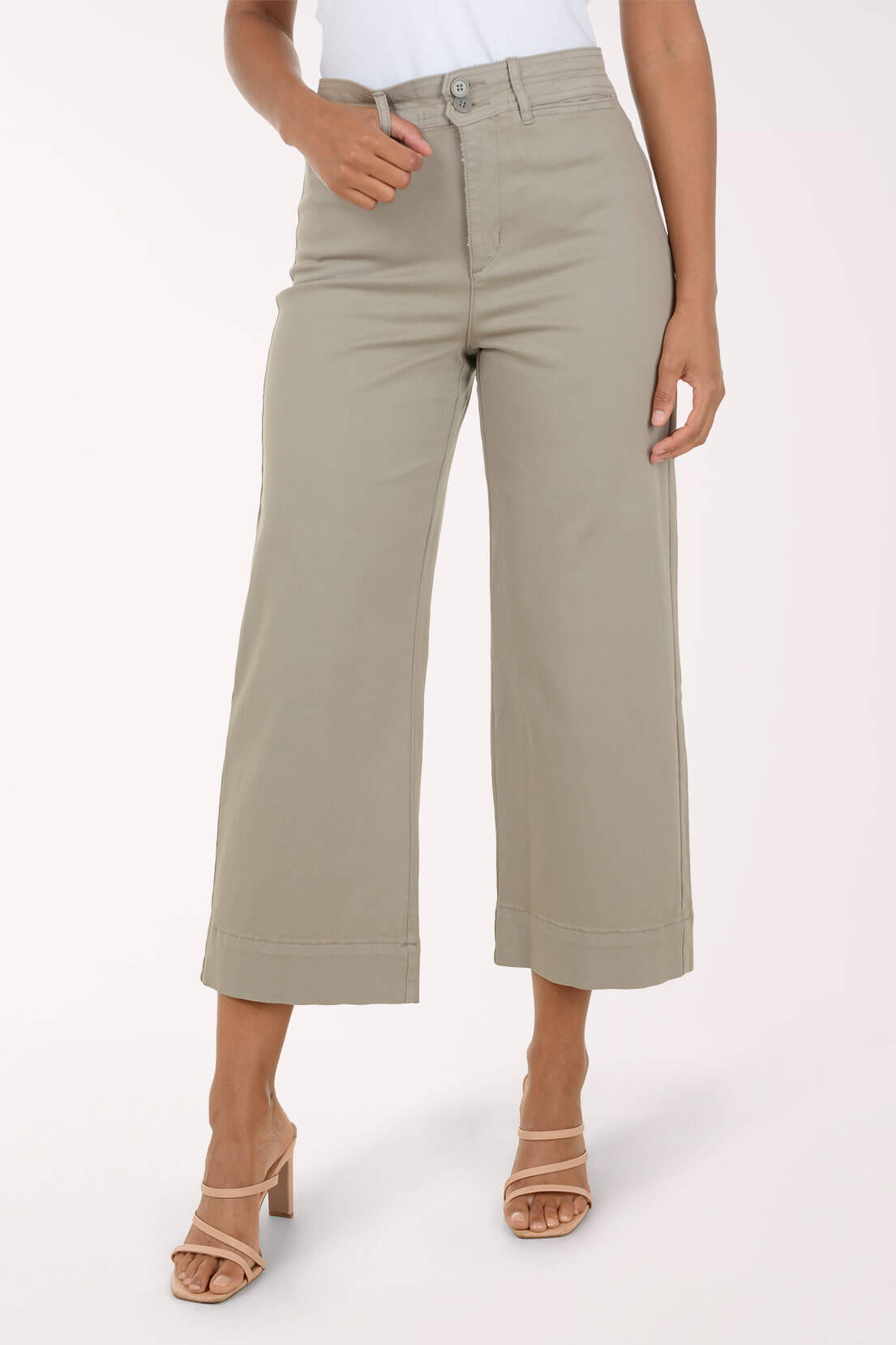 A model wearing a pair of light sage green cropped pants with a rolled hem, paired with beige strappy high-heeled sandals, against a plain off-white studio background.