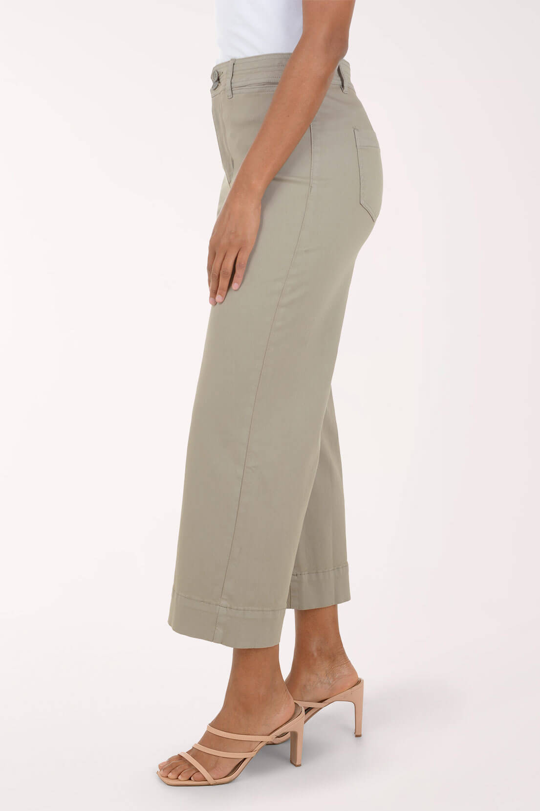 A model wearing a pair of light sage green cropped pants with a rolled hem, paired with beige strappy high-heeled sandals, against a plain off-white studio background.