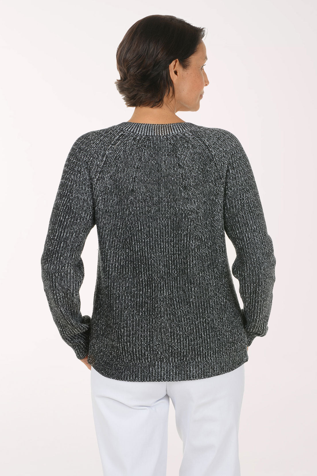 A smiling woman wearing a dark gray and black marled knit cardigan with brown buttons over a white top and white pants, photographed against a plain light background.