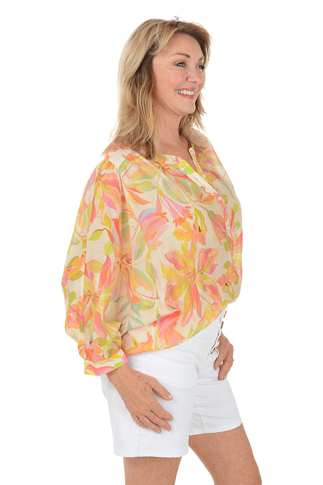 Woman wearing a colorful floral blouse and white shorts on a white background
