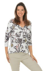 A front shot of a model wearing a floral v-neck knit top with 3/4 dolman sleeves and a straight hemline with side slits. The top is primarily white with a multicolor floral pattern.