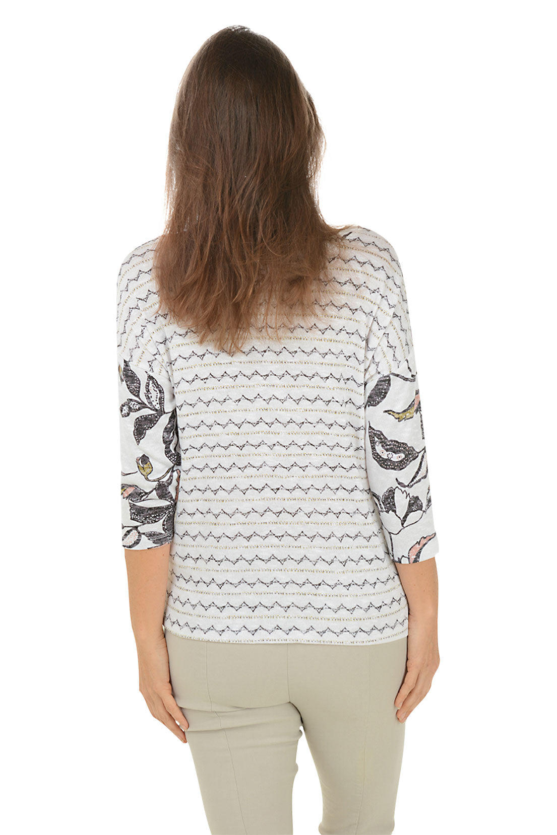 A back shot of a model wearing a floral v-neck knit top with 3/4 dolman sleeves and a straight hemline with side slits. The top is primarily white with a multicolor floral pattern.