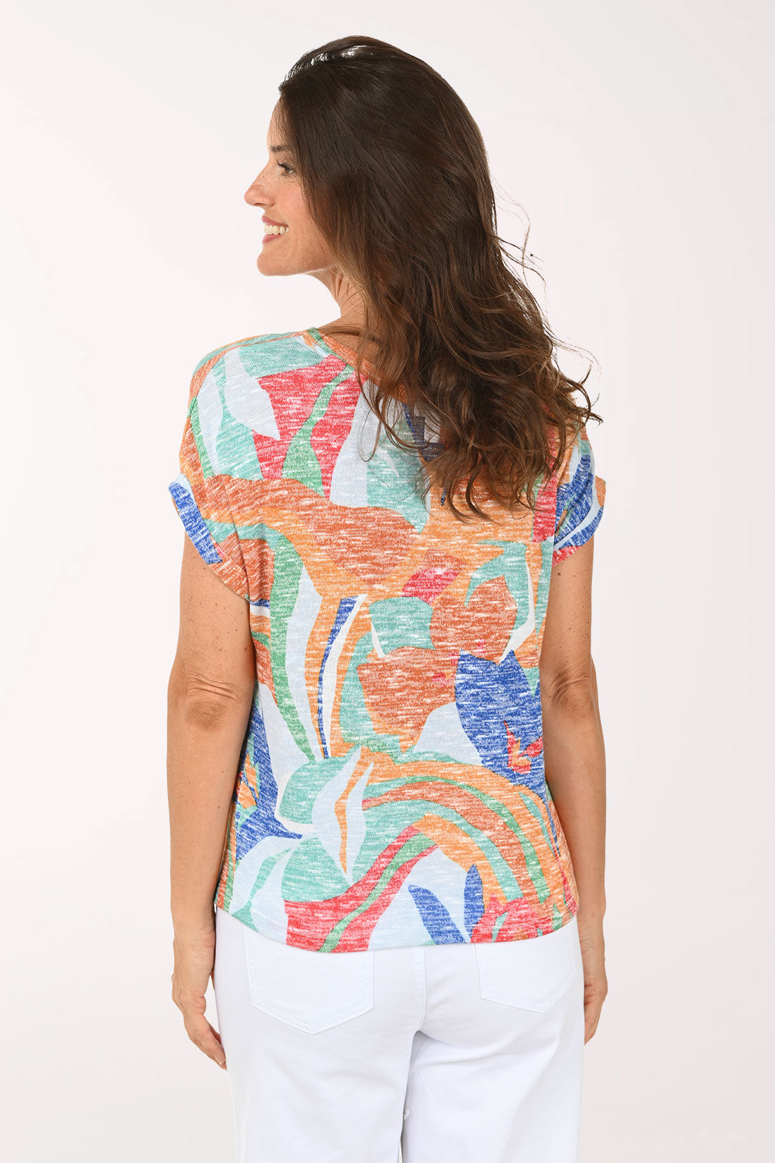 Woman wearing a colorful patterned top and white pants on a white background