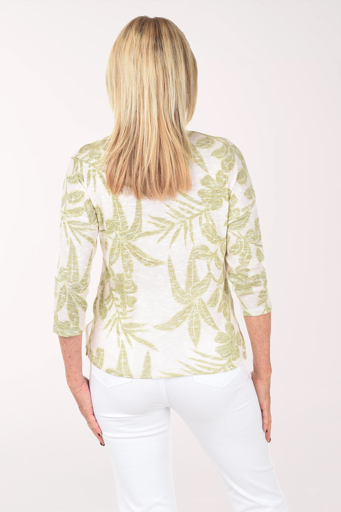 Woman wearing a light green and white patterned top with white pants on a white background