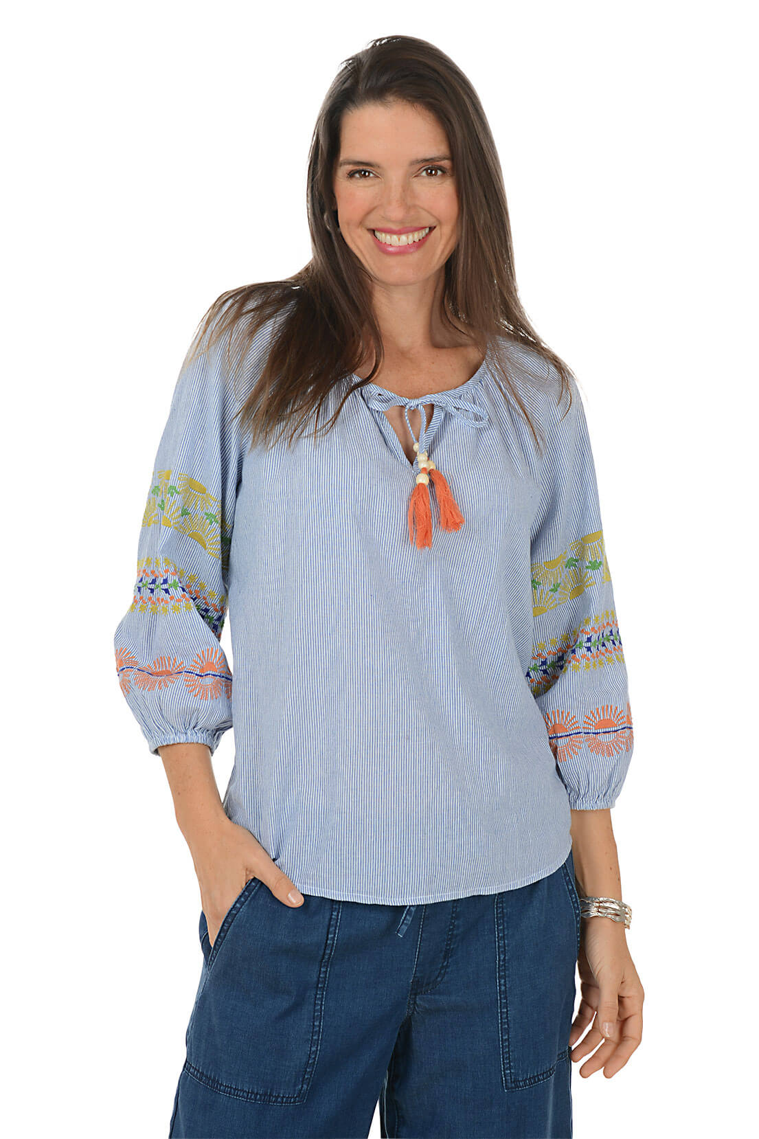 Woman wearing a light blue blouse with colorful patterns and orange tassels on a white background