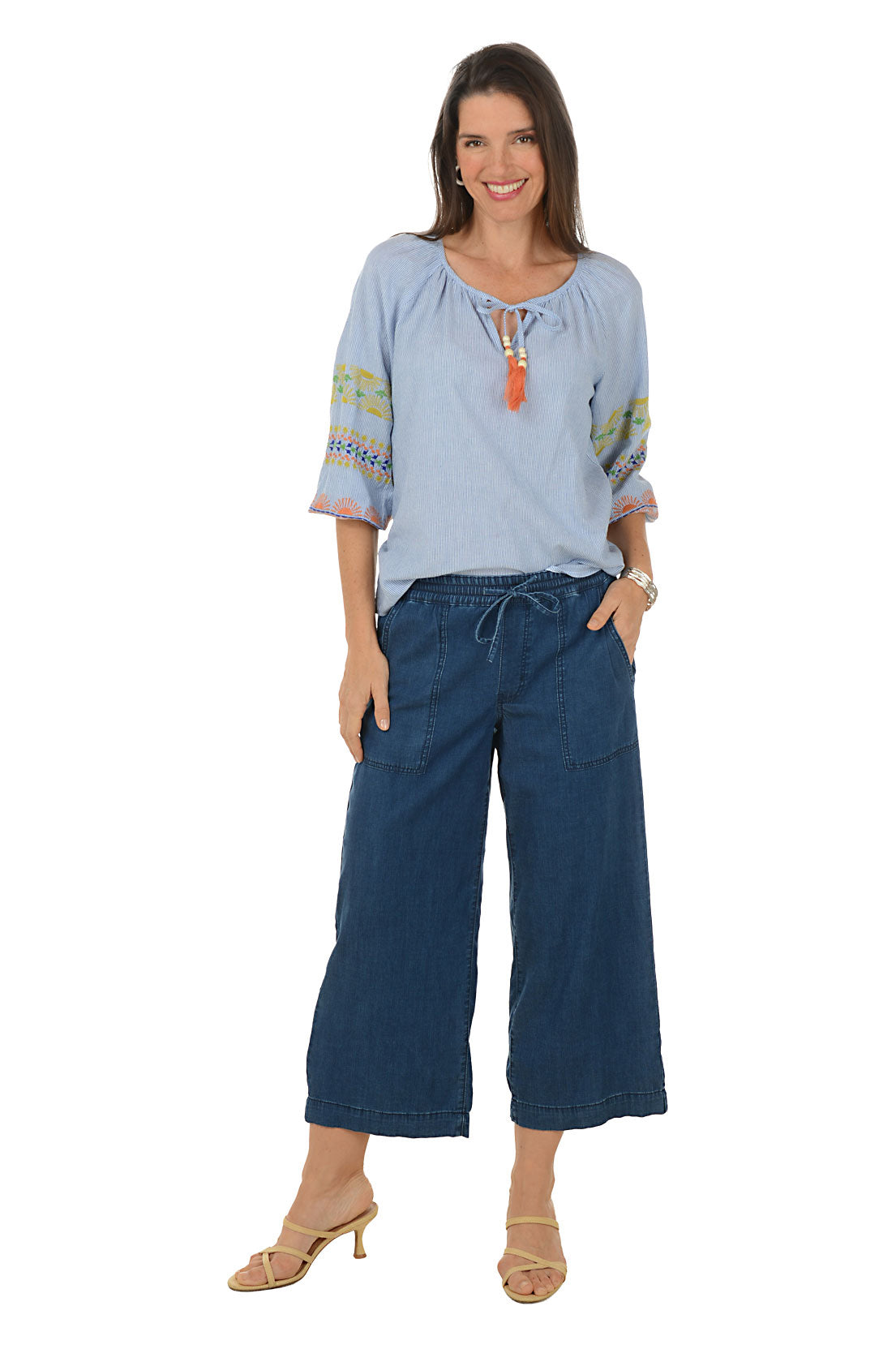 Woman wearing a light blue top with colorful accents and blue jeans on a white background