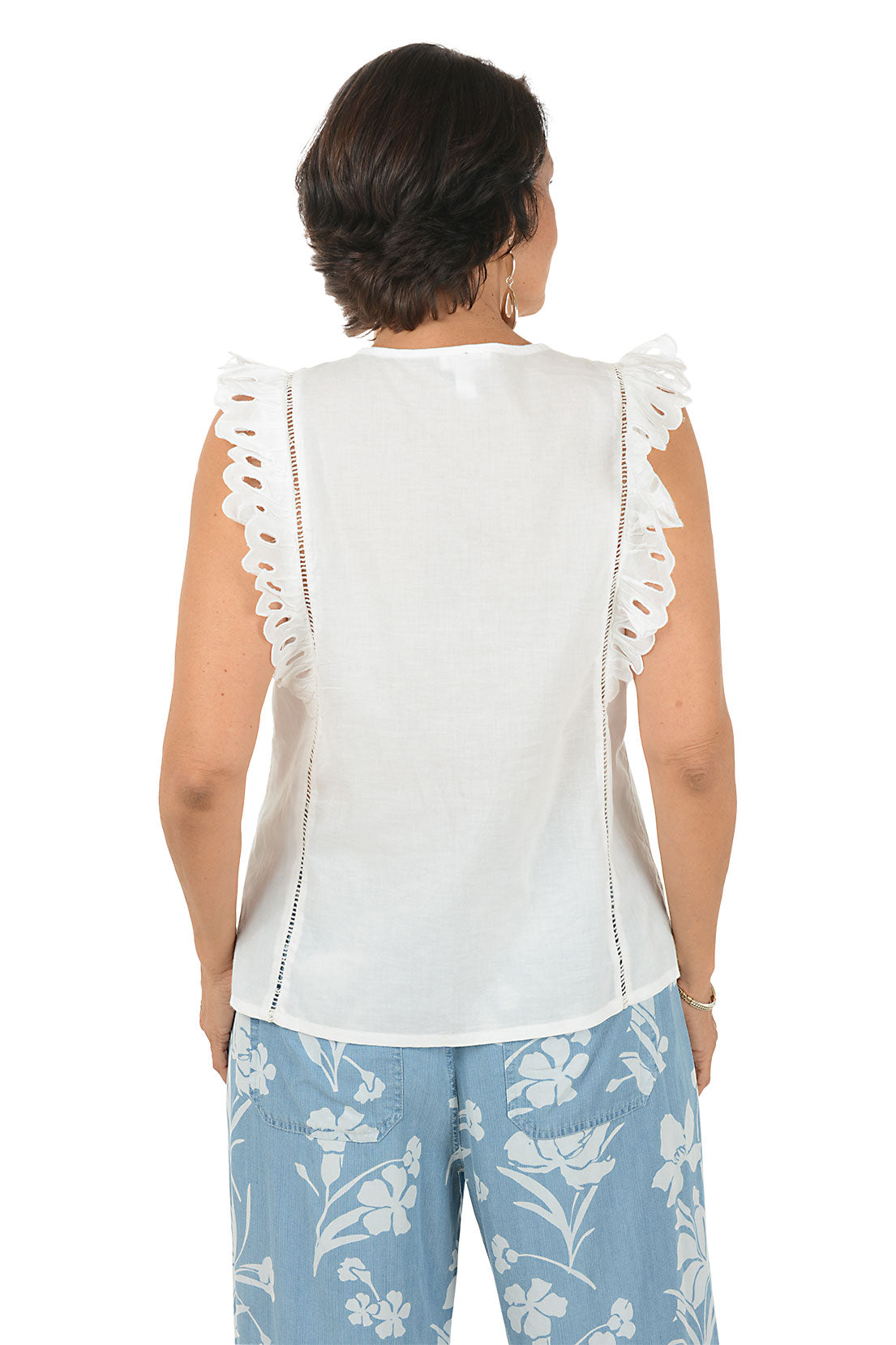 Woman wearing a white sleeveless top with lace details and blue floral pants on a white background